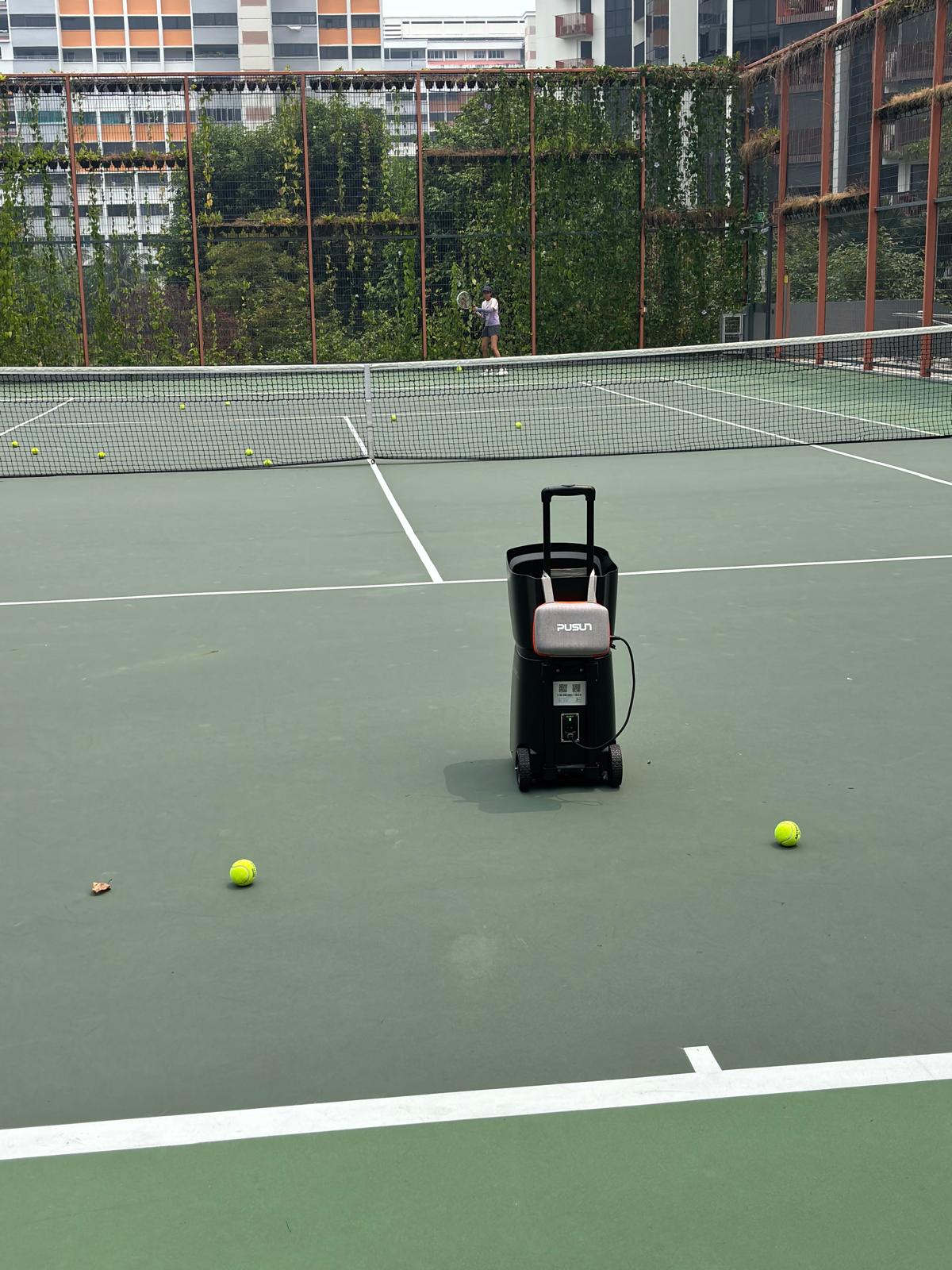 PUSUN ball machine on court while a player rallies from the baseline